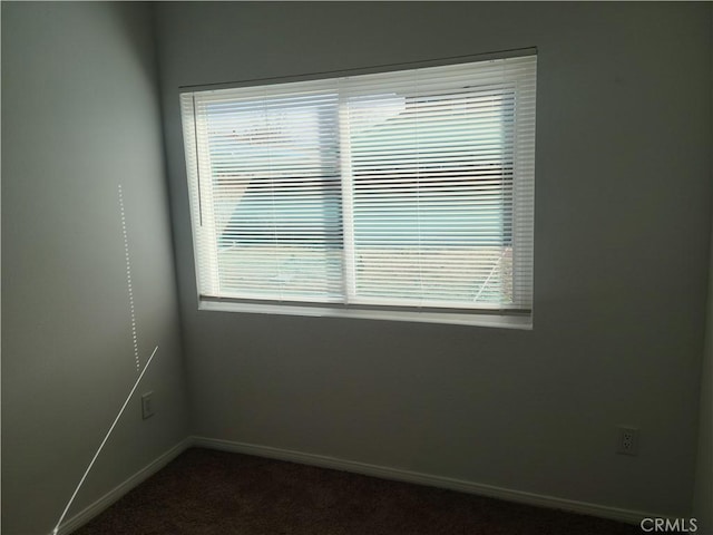 spare room featuring dark carpet and baseboards