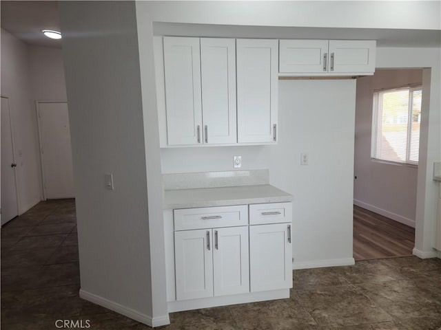 kitchen with white cabinetry, light countertops, dark tile patterned flooring, and baseboards