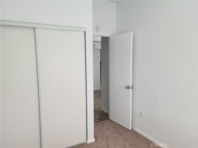 unfurnished bedroom featuring a closet, light colored carpet, and baseboards