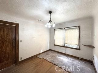 unfurnished room with a notable chandelier, wood finished floors, baseboards, and a textured ceiling