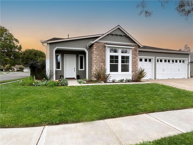 view of front of property featuring a front yard, decorative driveway, stone siding, and an attached garage