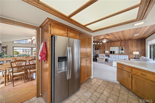 kitchen featuring open floor plan, wood walls, brown cabinetry, stainless steel fridge with ice dispenser, and tile counters