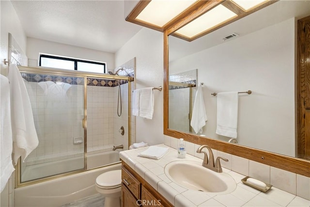 bathroom featuring visible vents, combined bath / shower with glass door, toilet, and vanity