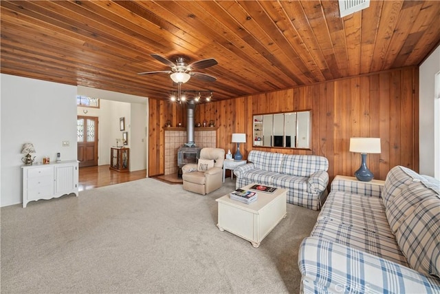 living area featuring visible vents, wooden walls, wood ceiling, carpet flooring, and a wood stove