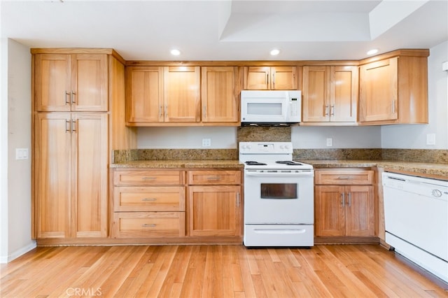 kitchen featuring white appliances, light stone countertops, light wood finished floors, a tray ceiling, and recessed lighting