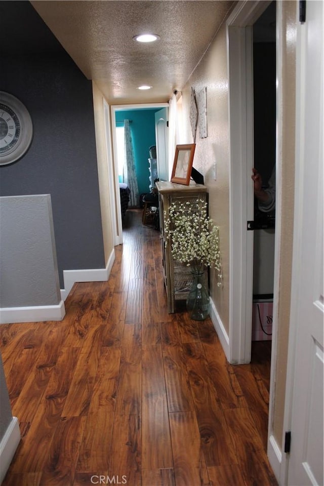 corridor with baseboards, a textured ceiling, and hardwood / wood-style flooring