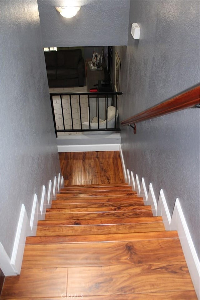 stairway with a textured ceiling, wood finished floors, and a textured wall