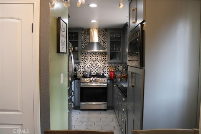 kitchen featuring light tile patterned floors, built in microwave, stainless steel stove, dark countertops, and wall chimney exhaust hood