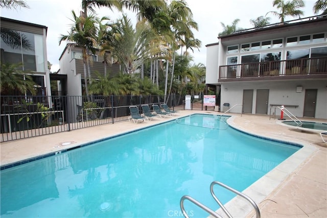 pool with a patio, a community hot tub, and fence