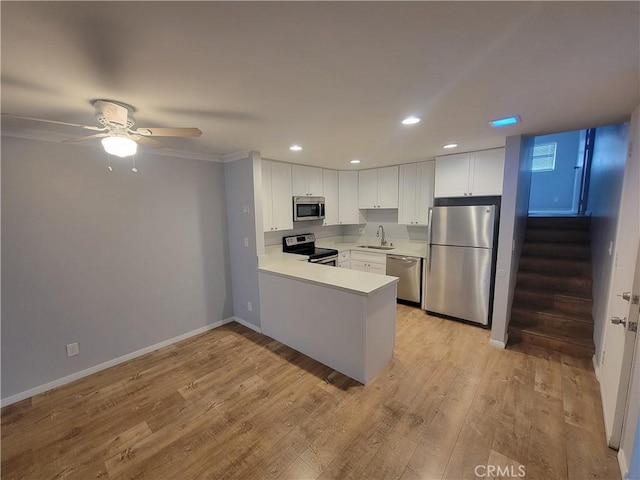 kitchen with light wood-type flooring, a sink, stainless steel appliances, a peninsula, and white cabinets