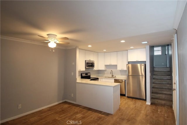 kitchen featuring a sink, wood finished floors, stainless steel appliances, a peninsula, and light countertops