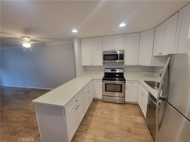 kitchen featuring light countertops, a peninsula, stainless steel appliances, light wood-style floors, and white cabinetry