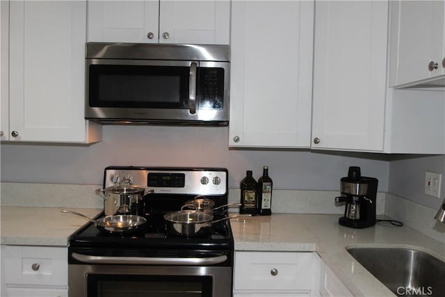 kitchen with light stone countertops, white cabinetry, stainless steel appliances, and a sink