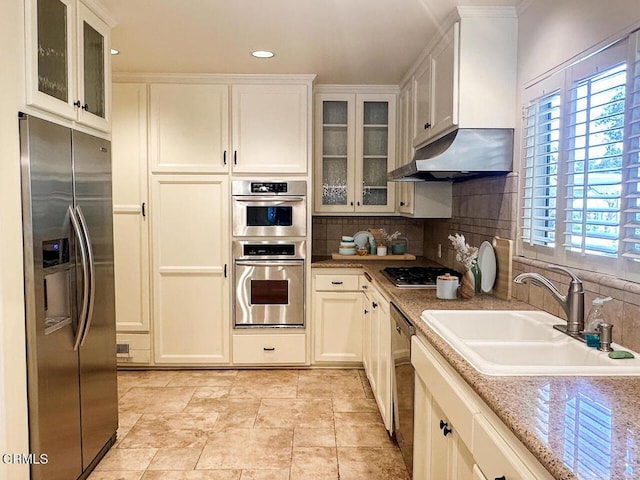 kitchen with a wealth of natural light, a sink, under cabinet range hood, backsplash, and stainless steel appliances