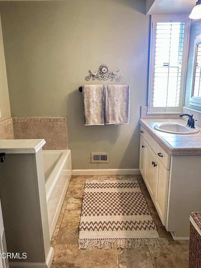 full bathroom with a bath, visible vents, vanity, and baseboards