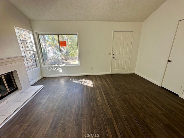 unfurnished living room featuring baseboards, lofted ceiling, dark wood-style flooring, a textured ceiling, and a tiled fireplace