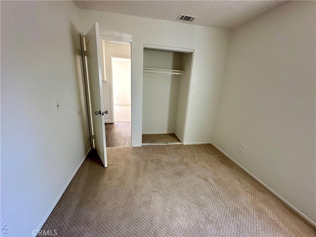 unfurnished bedroom featuring visible vents, a textured ceiling, a closet, carpet, and baseboards