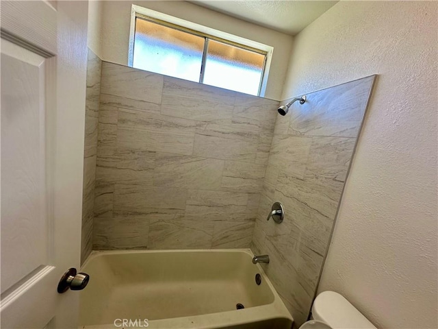 bathroom featuring tub / shower combination, toilet, and a textured wall