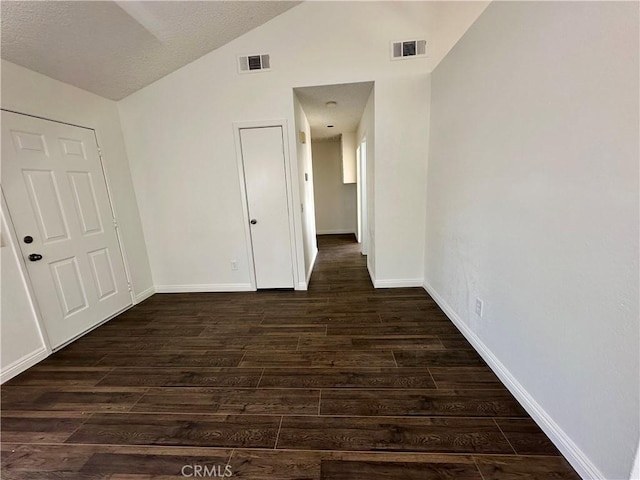 unfurnished room featuring vaulted ceiling, dark wood-style floors, visible vents, and baseboards