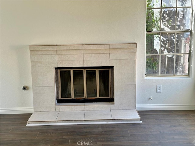 room details featuring a tiled fireplace, baseboards, and wood finished floors