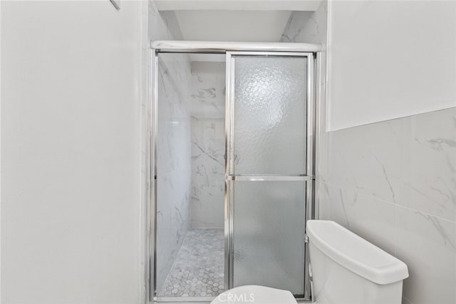 full bathroom with a marble finish shower, toilet, and tile walls