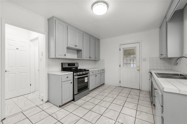 kitchen with tile countertops, gray cabinets, a sink, decorative backsplash, and gas range