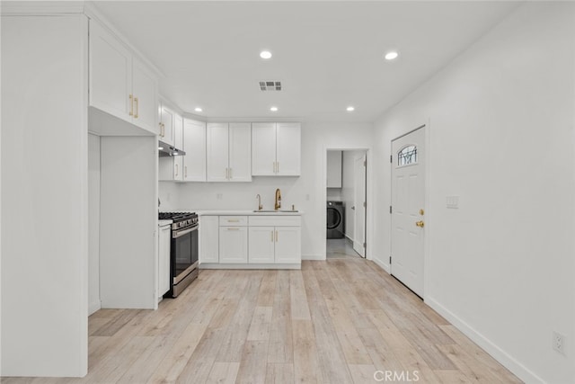 kitchen featuring visible vents, under cabinet range hood, stainless steel gas stove, washer / clothes dryer, and white cabinetry