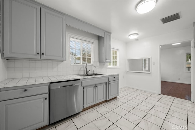 kitchen featuring visible vents, gray cabinets, a sink, stainless steel dishwasher, and tile countertops