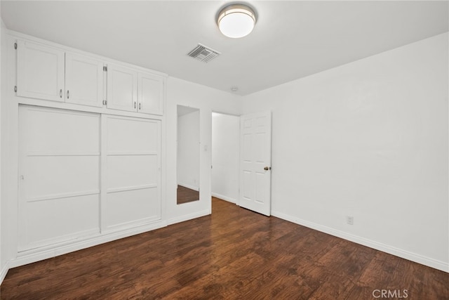 unfurnished bedroom featuring dark wood-type flooring, baseboards, visible vents, and a closet