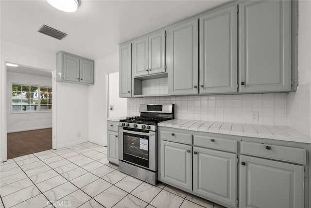 kitchen with visible vents, gas range, gray cabinetry, and tile counters