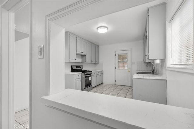 kitchen with a sink, stainless steel range with gas cooktop, light countertops, light tile patterned floors, and decorative backsplash