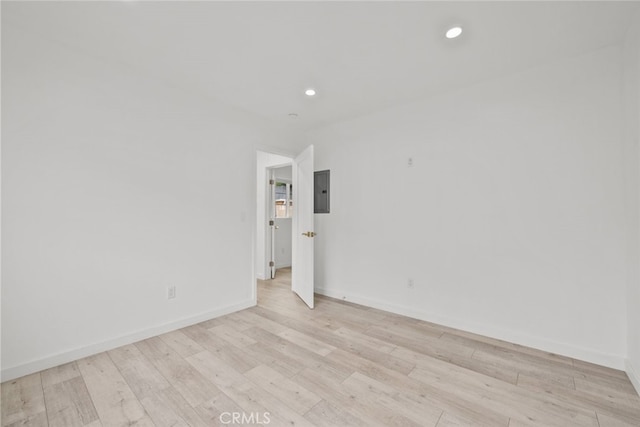 unfurnished room with light wood finished floors, recessed lighting, electric panel, and baseboards