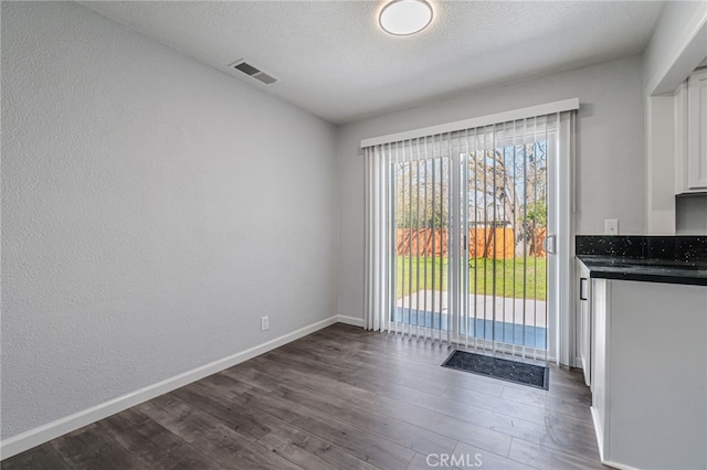 doorway to outside featuring visible vents, baseboards, dark wood finished floors, a textured wall, and a textured ceiling