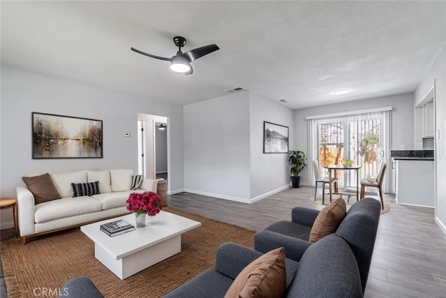 living area featuring ceiling fan, visible vents, baseboards, and wood finished floors