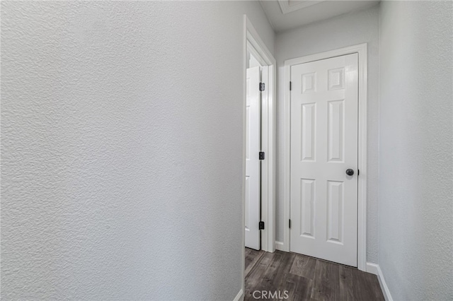 corridor with dark wood-style floors, baseboards, and a textured wall