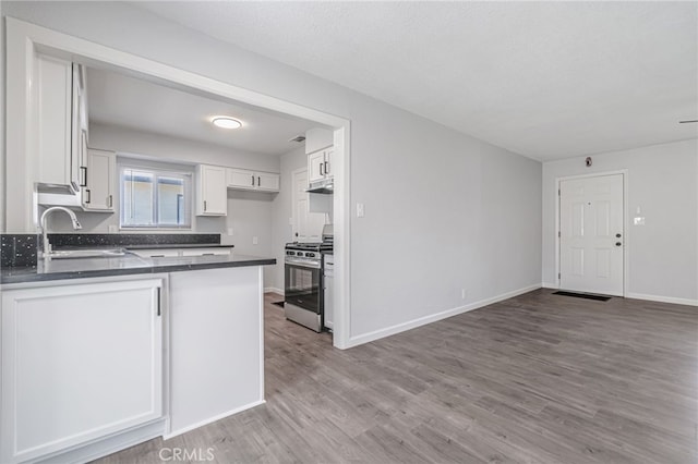 kitchen with a sink, dark countertops, white cabinetry, a peninsula, and gas range