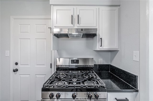 kitchen featuring under cabinet range hood, gas range, dark stone counters, a textured wall, and white cabinets