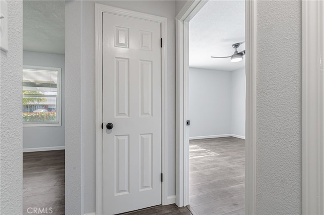 hallway featuring wood finished floors, baseboards, a textured wall, and a textured ceiling