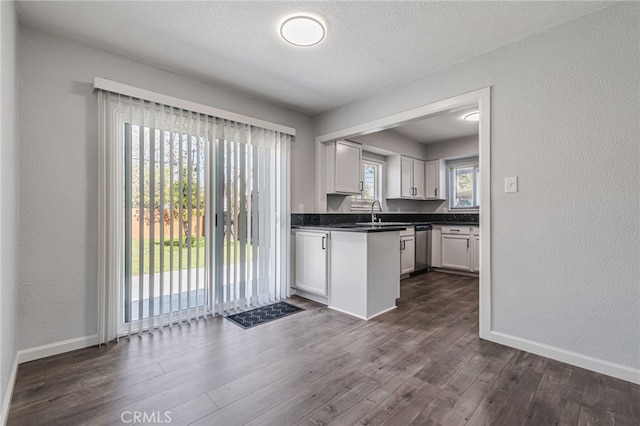 kitchen with dark wood-style floors, baseboards, dishwasher, white cabinetry, and dark countertops