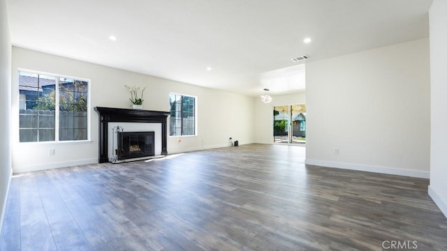 unfurnished living room with a glass covered fireplace, wood finished floors, visible vents, and baseboards