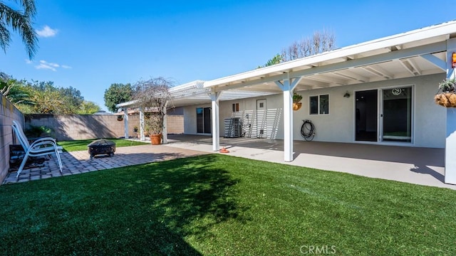 back of house featuring stucco siding, a lawn, a patio, fence, and an outdoor fire pit