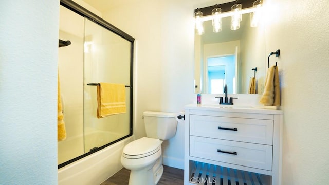 bathroom featuring vanity, wood finished floors, baseboards, bath / shower combo with glass door, and toilet