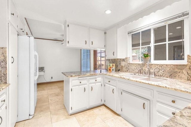 kitchen with tasteful backsplash, a peninsula, freestanding refrigerator, white cabinetry, and a sink