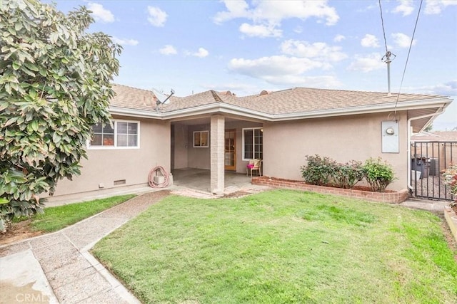 rear view of house with a patio, a lawn, fence, and stucco siding