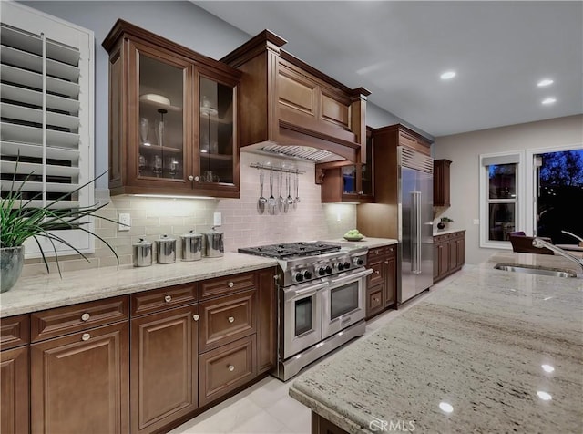 kitchen with light stone counters, premium appliances, backsplash, and a sink