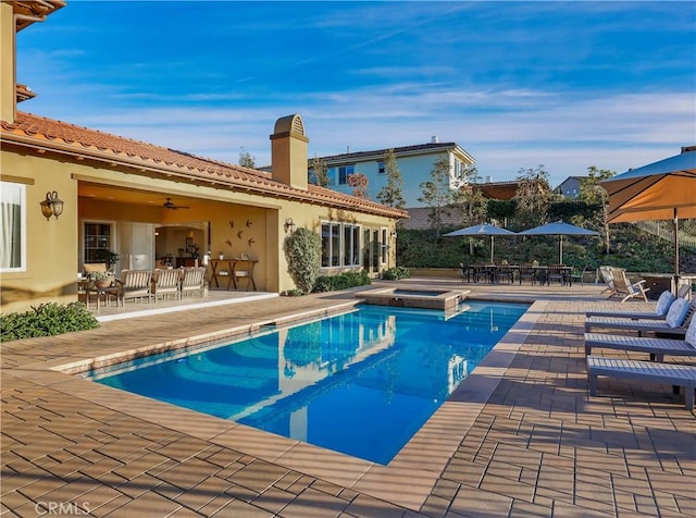 view of swimming pool with ceiling fan, a pool with connected hot tub, outdoor dining area, and a patio