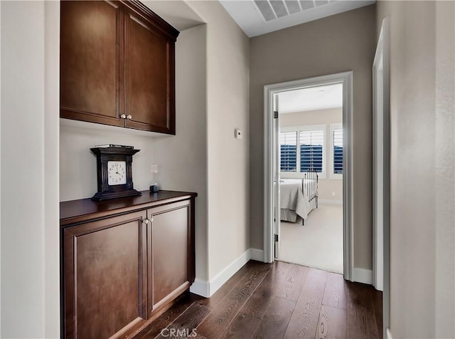 hallway featuring visible vents, baseboards, and dark wood finished floors