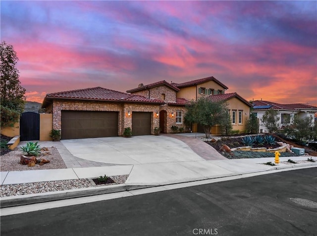 view of front of property with a tiled roof, a garage, stone siding, driveway, and a gate