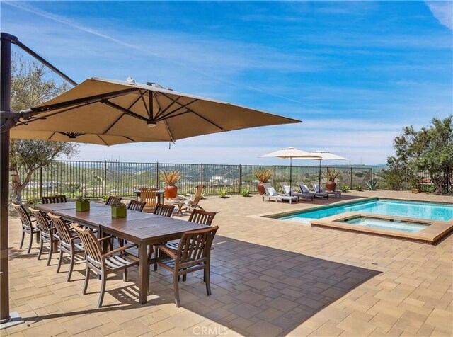view of pool featuring a pool with connected hot tub, fence, outdoor dining area, and a patio area