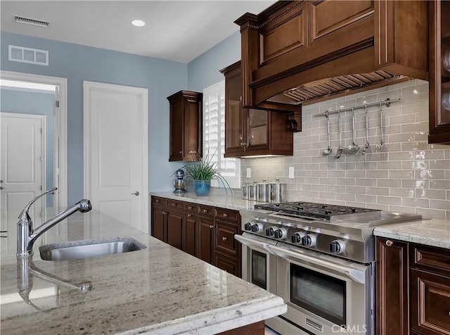 kitchen with visible vents, a sink, decorative backsplash, and range with two ovens